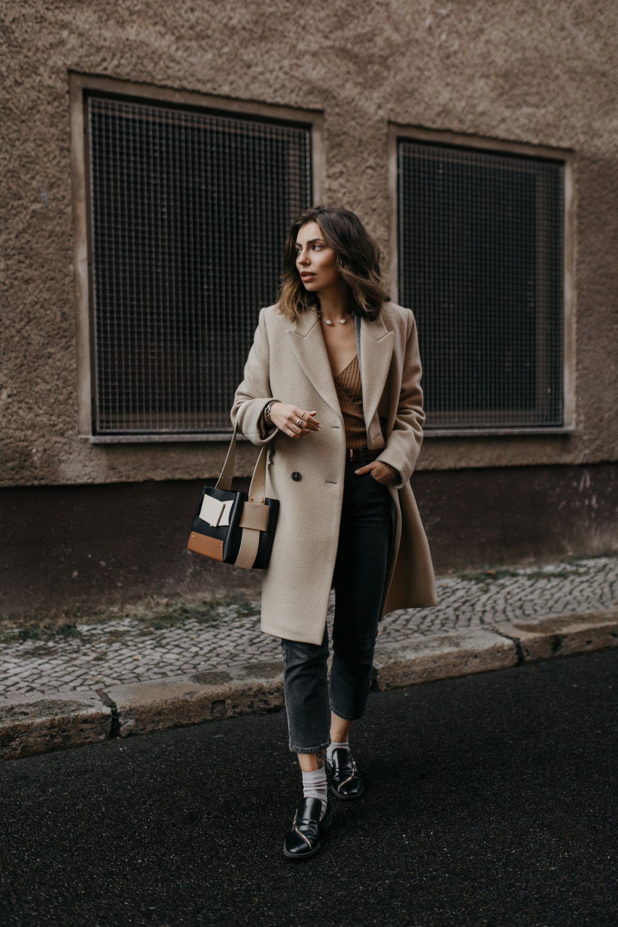 Streetstyle by Masha Sedgwick | Early spring city outfit inspiration, wearing beige classic Closed coat, beige-brown-black Yuzefi shoulder bag, grey Closed jeans, black &other Stories loafer with zipper, grey socks, grey Gestuz blazer, wrapped brown Baum & Pferdgarten shirt | Berlin street style editorial shooting