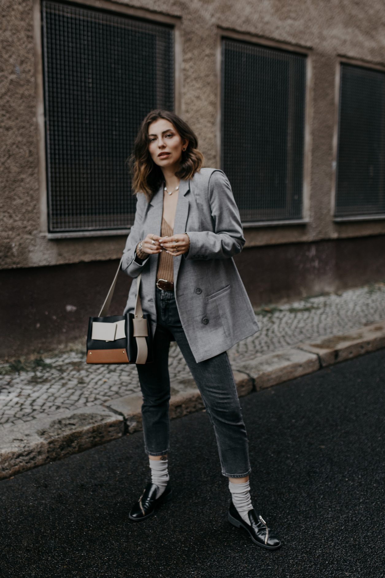 Streetstyle by Masha Sedgwick | Early spring city outfit inspiration, wearing beige classic Closed coat, beige-brown-black Yuzefi shoulder bag, grey Closed jeans, black &other Stories loafer with zipper, grey socks, grey Gestuz blazer, wrapped brown Baum & Pferdgarten shirt | Berlin street style editorial shooting