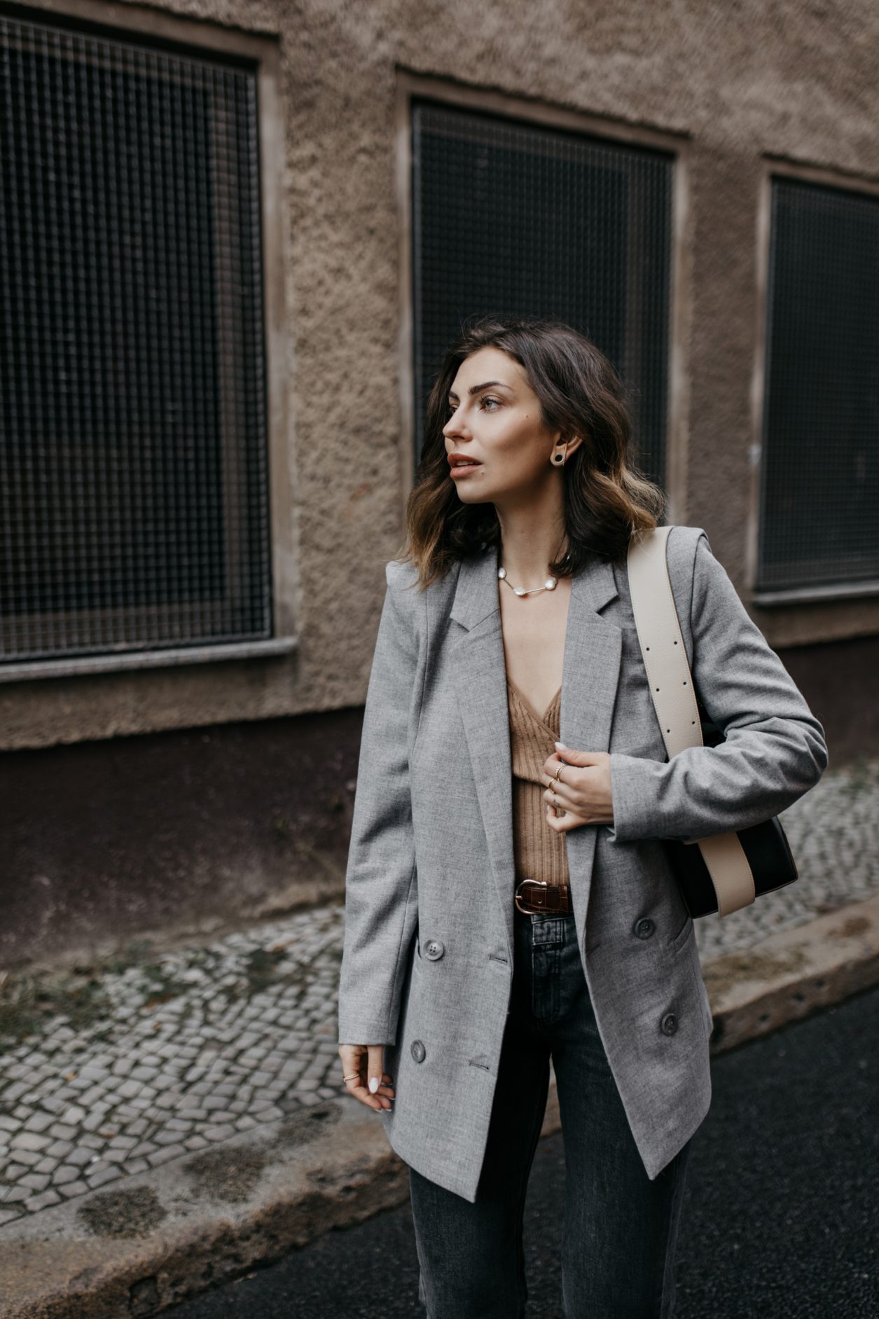 Streetstyle by Masha Sedgwick | Early spring city outfit inspiration, wearing beige classic Closed coat, beige-brown-black Yuzefi shoulder bag, grey Closed jeans, black &other Stories loafer with zipper, grey socks, grey Gestuz blazer, wrapped brown Baum & Pferdgarten shirt | Berlin street style editorial shooting
