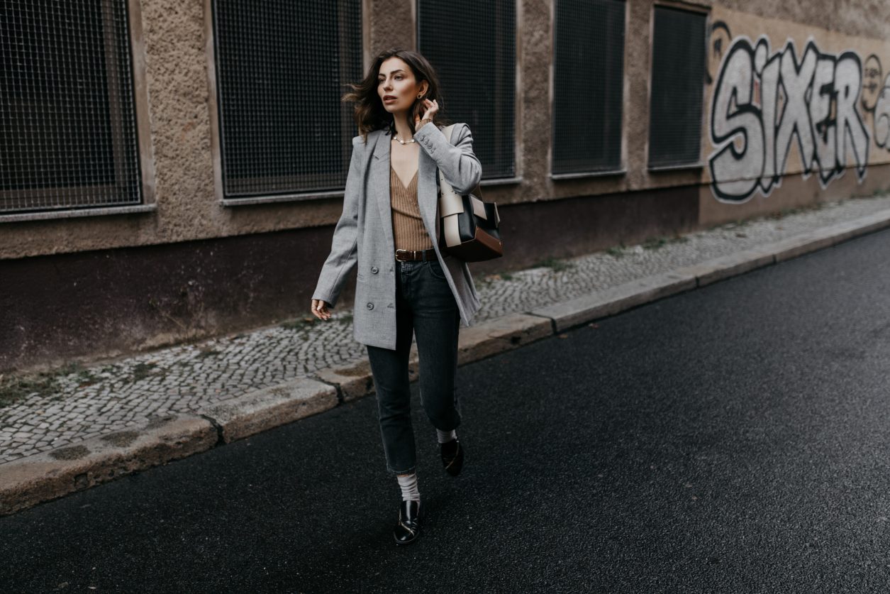 Streetstyle by Masha Sedgwick | Early spring city outfit inspiration, wearing beige classic Closed coat, beige-brown-black Yuzefi shoulder bag, grey Closed jeans, black &other Stories loafer with zipper, grey socks, grey Gestuz blazer, wrapped brown Baum & Pferdgarten shirt | Berlin street style editorial shooting