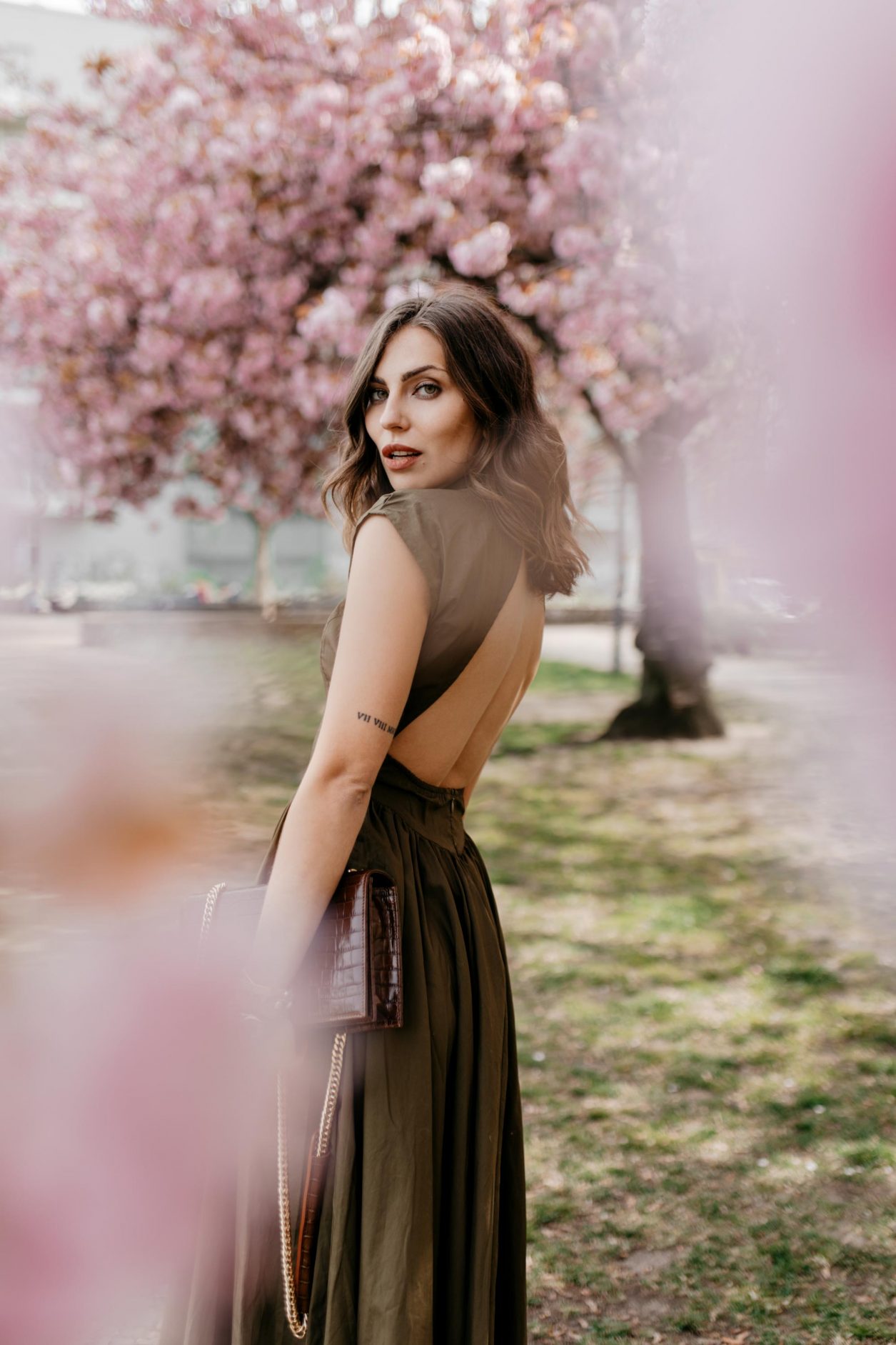 Anzeige | Streetstyle by fashion blogger Masha Sedgwick | Wearing khaki green midi dress with open back by Gestuz, black heeled sandals from Office via Zalando, brown leather cross-body bag with golden chain from Agneel | Minimalistic effortless cool outfit, city chic look, shooting spot: Berlin, cherry blossom