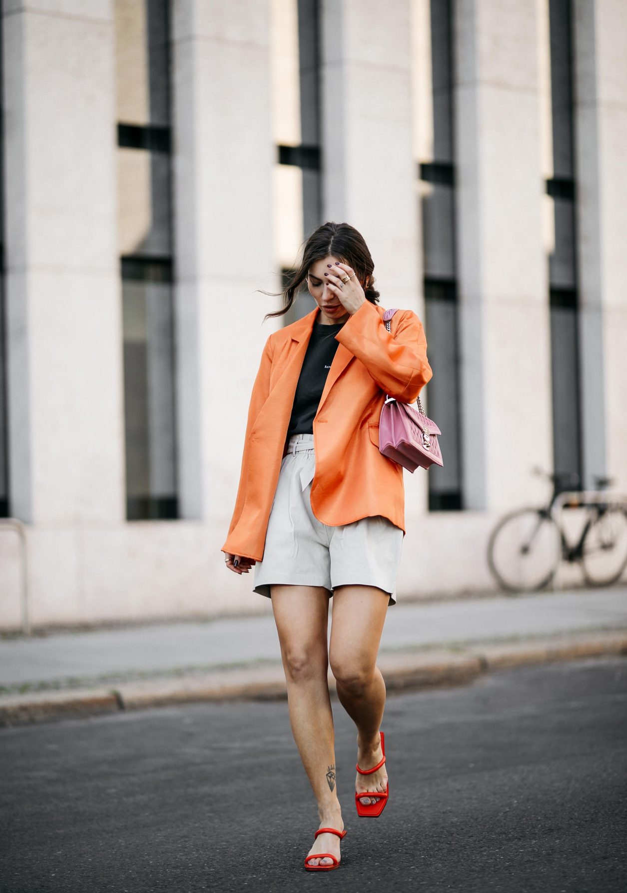 Summer Streetstyle Look by Masha Sedgwick | Photographer: Jeremy Moeller | Summer style trends & outfit inspiration, fashion blogger from Berlin, Germany | Wearing orange Baum Pferdgarten Blazer, graphic grey Acne Studios logo shirt, white leather Copenhagen Muse paperboy shorts, pink Miu Miu shoulder bag, red straps sandals by Charles & Keith | Hair style: messy ponytail