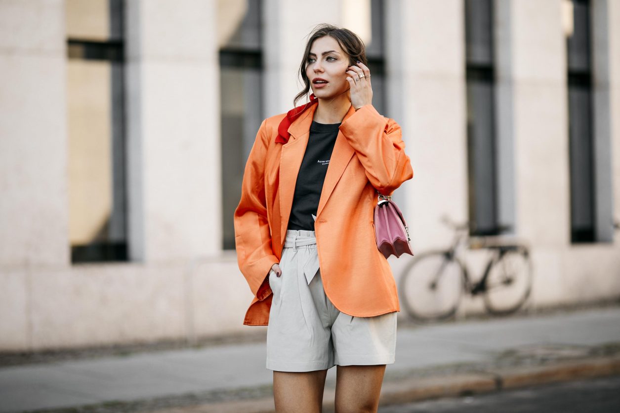 Summer Streetstyle Look by Masha Sedgwick | Photographer: Jeremy Moeller | Summer style trends & outfit inspiration, fashion blogger from Berlin, Germany | Wearing orange Baum Pferdgarten Blazer, graphic grey Acne Studios logo shirt, white leather Copenhagen Muse paperboy shorts, pink Miu Miu shoulder bag, red straps sandals by Charles & Keith | Hair style: messy ponytail