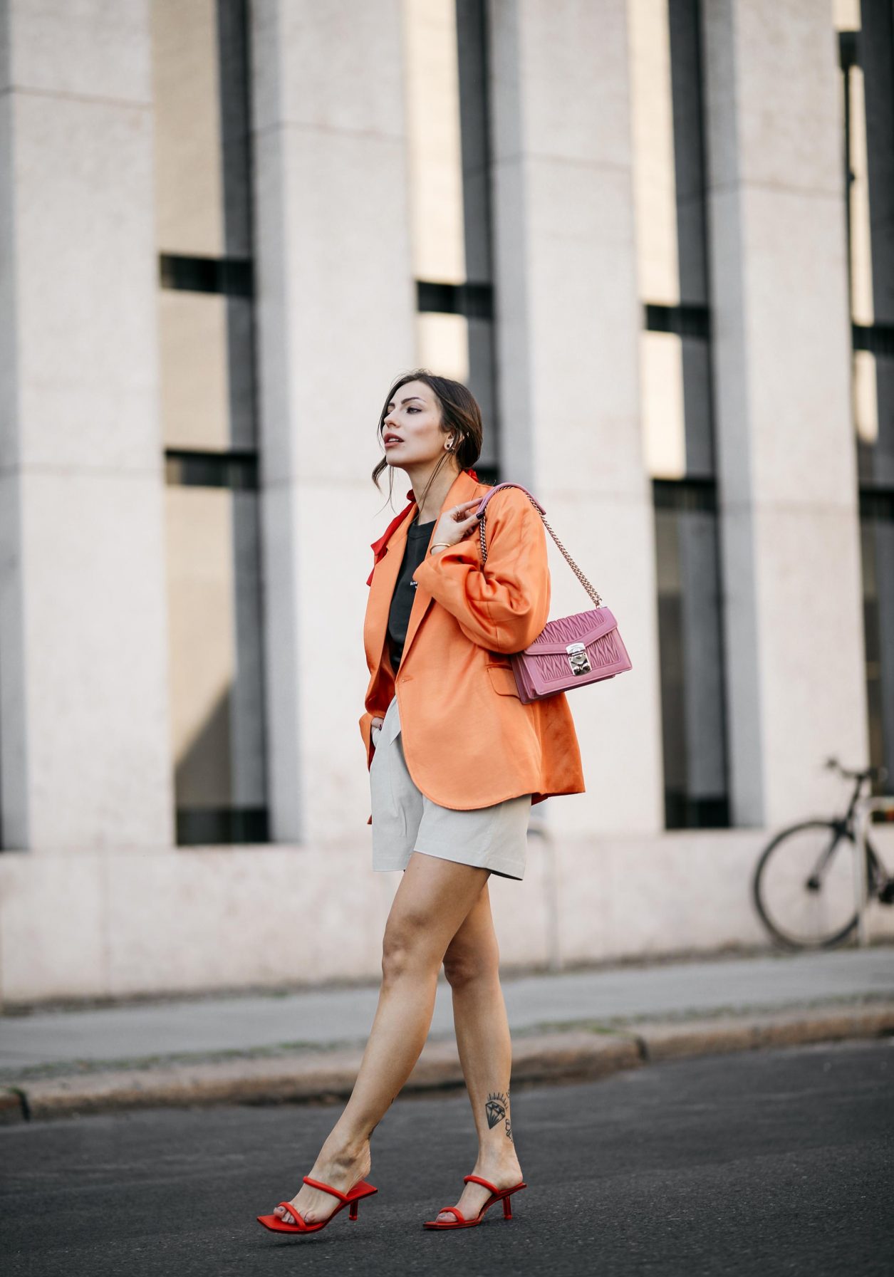 Summer Streetstyle Look by Masha Sedgwick | Photographer: Jeremy Moeller | Summer style trends & outfit inspiration, fashion blogger from Berlin, Germany | Wearing orange Baum Pferdgarten Blazer, graphic grey Acne Studios logo shirt, white leather Copenhagen Muse paperboy shorts, pink Miu Miu shoulder bag, red straps sandals by Charles & Keith | Hair style: messy ponytail