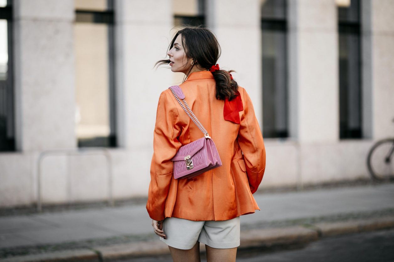 Summer Streetstyle Look by Masha Sedgwick | Photographer: Jeremy Moeller | Summer style trends & outfit inspiration, fashion blogger from Berlin, Germany | Wearing orange Baum Pferdgarten Blazer, graphic grey Acne Studios logo shirt, white leather Copenhagen Muse paperboy shorts, pink Miu Miu shoulder bag, red straps sandals by Charles & Keith | Hair style: messy ponytail