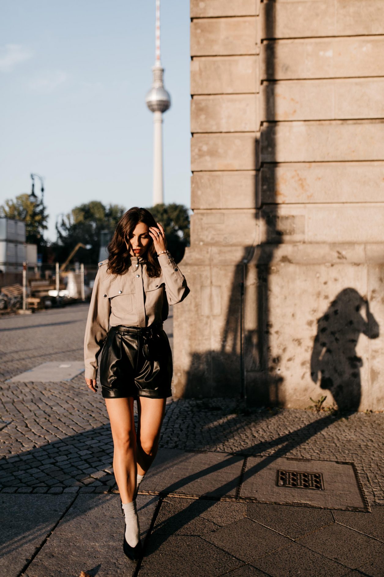 Berlin fashion and beauty blogger Masha Sedgwick, early autumn sustainable outfit inspiration: bleck faux leather Gestuz shorts, black leather Polene Paris belt bag, grey Designers Remix military blouse, grey socks, black Charles Keith slingback | Photo spot: Berlin Nikolaiviertel, streetstyle photographer Tonya Matyu