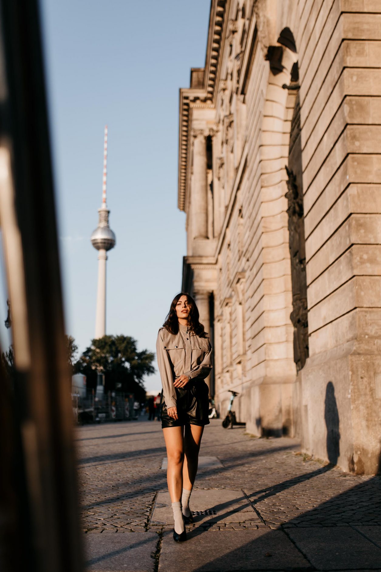 Berlin fashion and beauty blogger Masha Sedgwick, early autumn sustainable outfit inspiration: bleck faux leather Gestuz shorts, black leather Polene Paris belt bag, grey Designers Remix military blouse, grey socks, black Charles Keith slingback | Photo spot: Berlin Nikolaiviertel, streetstyle photographer Tonya Matyu
