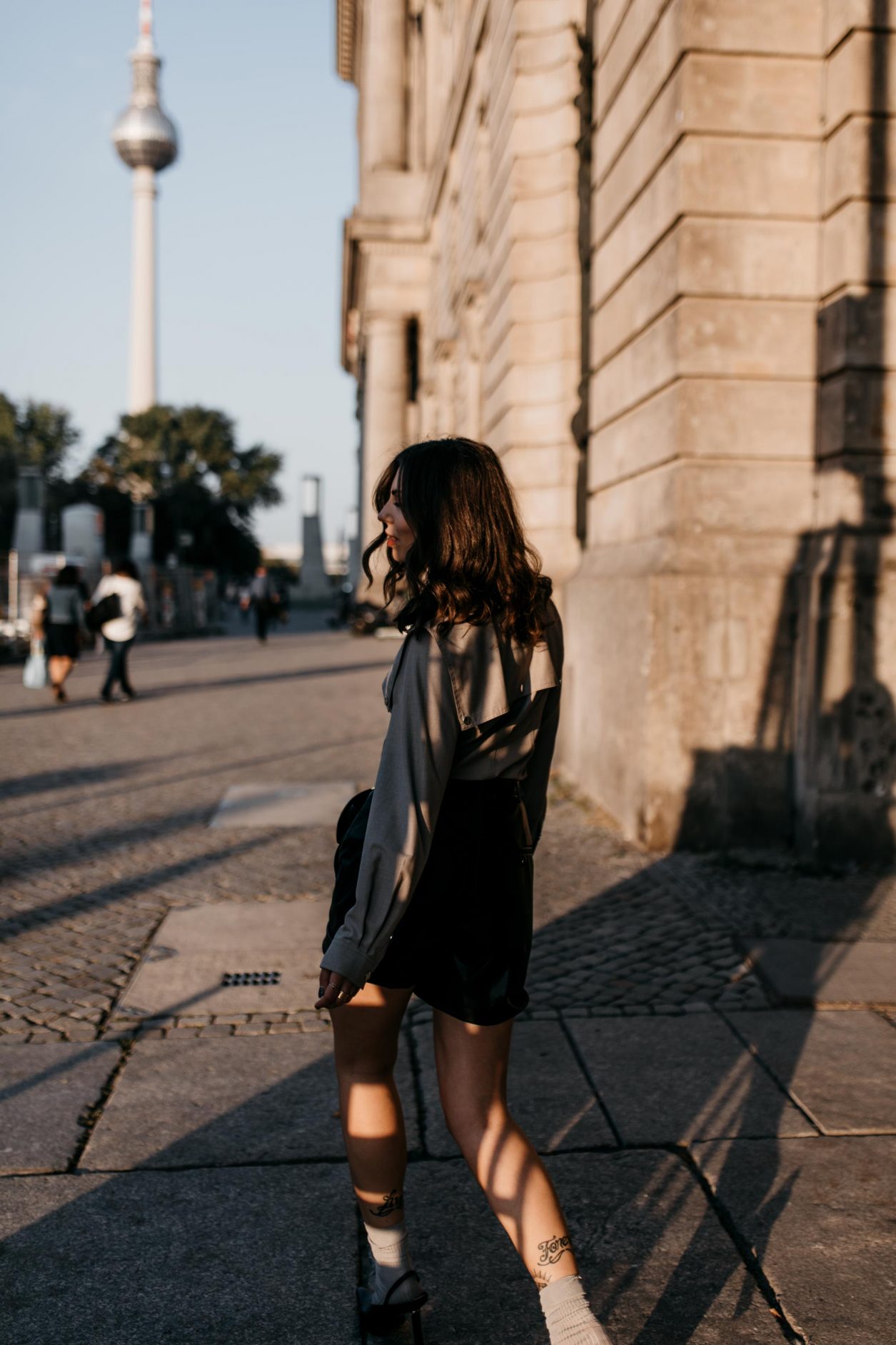 Berlin fashion and beauty blogger Masha Sedgwick, early autumn sustainable outfit inspiration: bleck faux leather Gestuz shorts, black leather Polene Paris belt bag, grey Designers Remix military blouse, grey socks, black Charles Keith slingback | Photo spot: Berlin Nikolaiviertel, streetstyle photographer Tonya Matyu