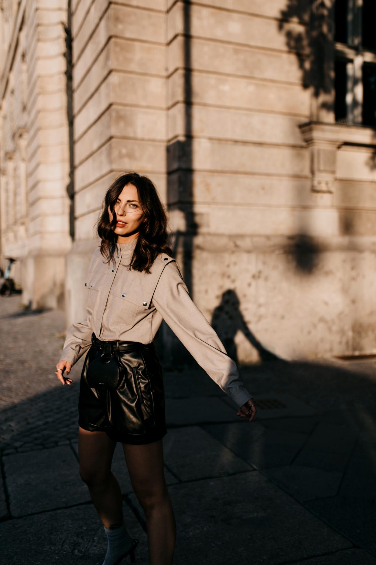 Berlin fashion and beauty blogger Masha Sedgwick, early autumn sustainable outfit inspiration: bleck faux leather Gestuz shorts, black leather Polene Paris belt bag, grey Designers Remix military blouse, grey socks, black Charles Keith slingback | Photo spot: Berlin Nikolaiviertel, streetstyle photographer Tonya Matyu
