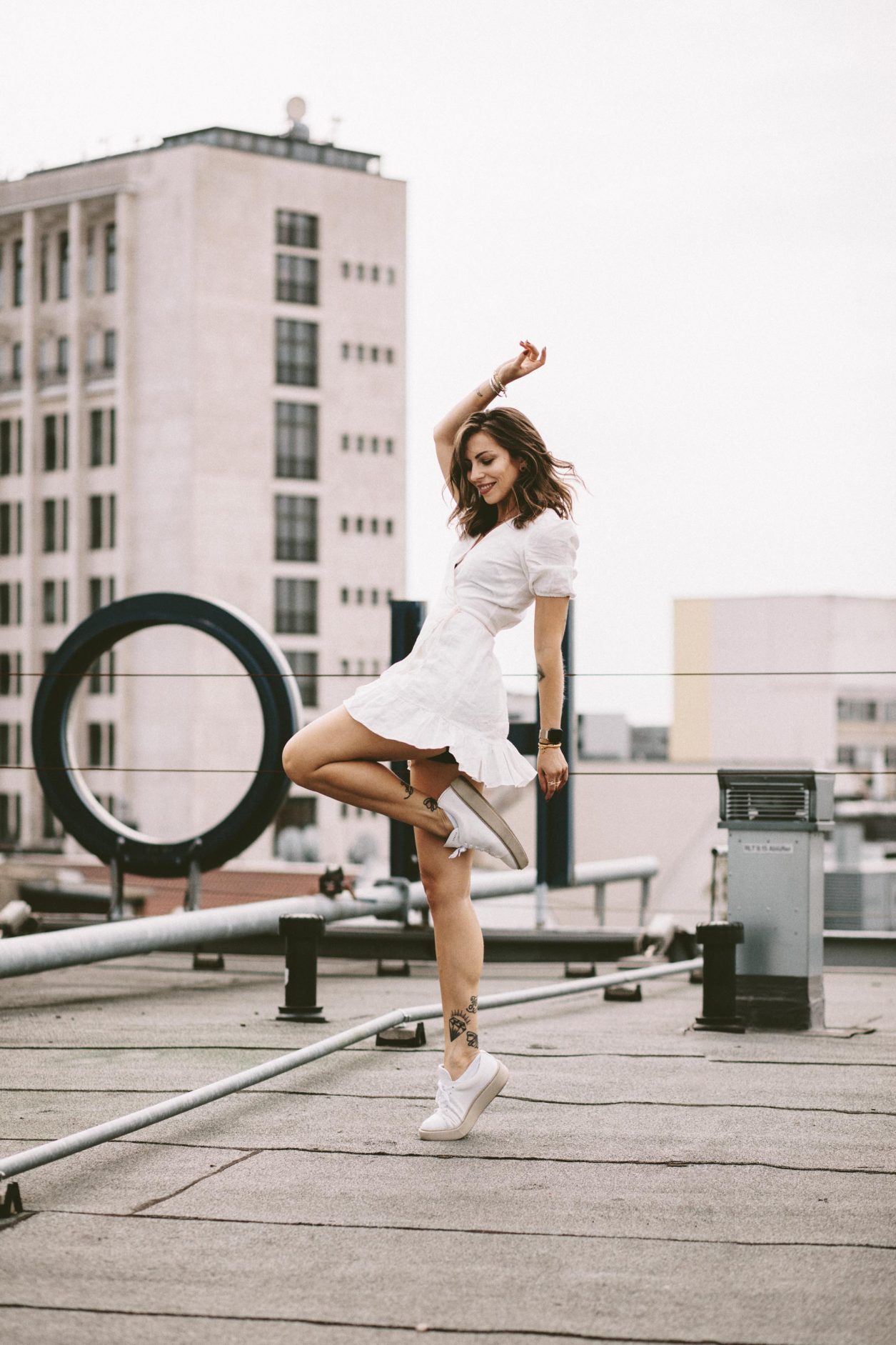 Anzeige | Fashion and beauty blogger from Berlin, Germany - Masha Sedgwick on the roof of Hotel Zoo, summer outfit inspiration: cute white linen wrapped mini dress, golden jewelry from Ariane Ernst, Thomas Sabo, Bulgari ring, white Coach sneaker | Inked fashion blogger, minimalistic, chic, effortless cool, streetstyle inspiration, ootd, photographer Tonya Matyu