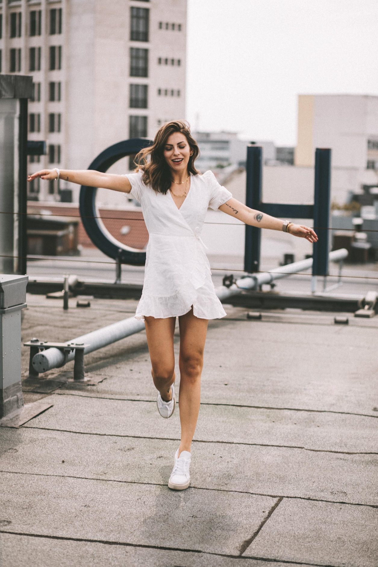 Anzeige | Fashion and beauty blogger from Berlin, Germany - Masha Sedgwick on the roof of Hotel Zoo, summer outfit inspiration: cute white linen wrapped mini dress, golden jewelry from Ariane Ernst, Thomas Sabo, Bulgari ring, white Coach sneaker | Inked fashion blogger, minimalistic, chic, effortless cool, streetstyle inspiration, ootd, photographer Tonya Matyu