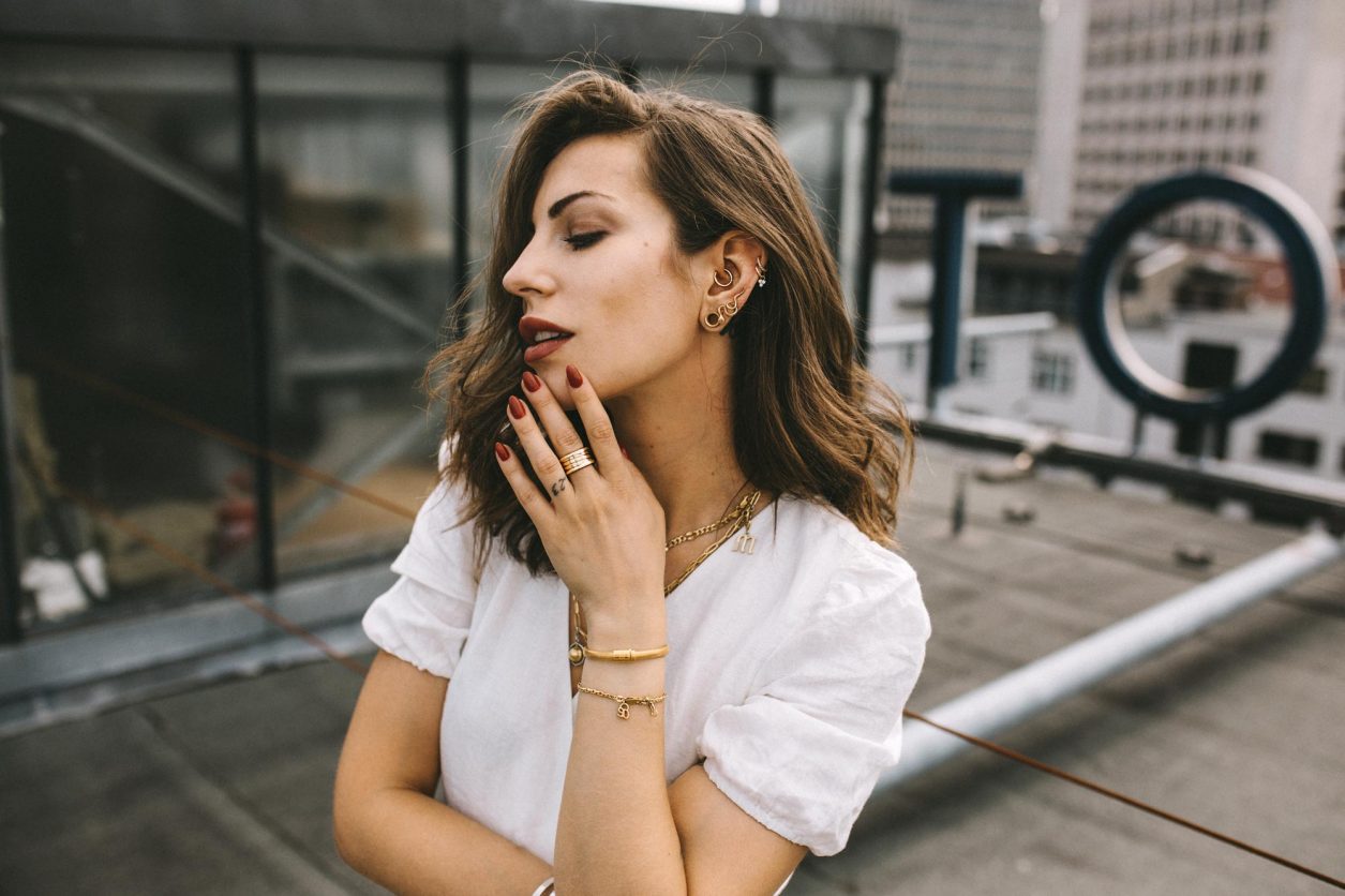 Anzeige | Portrait of fashion and beauty blogger from Berlin, Germany - Masha Sedgwick on the roof of Hotel Zoo, summer outfit inspiration: cute white linen wrapped mini dress, golden jewelry from Ariane Ernst, Thomas Sabo, Bulgari ring, white Coach sneaker | Inked fashion blogger, minimalistic, chic, effortless cool, streetstyle inspiration, ootd, photographer Tonya Matyu