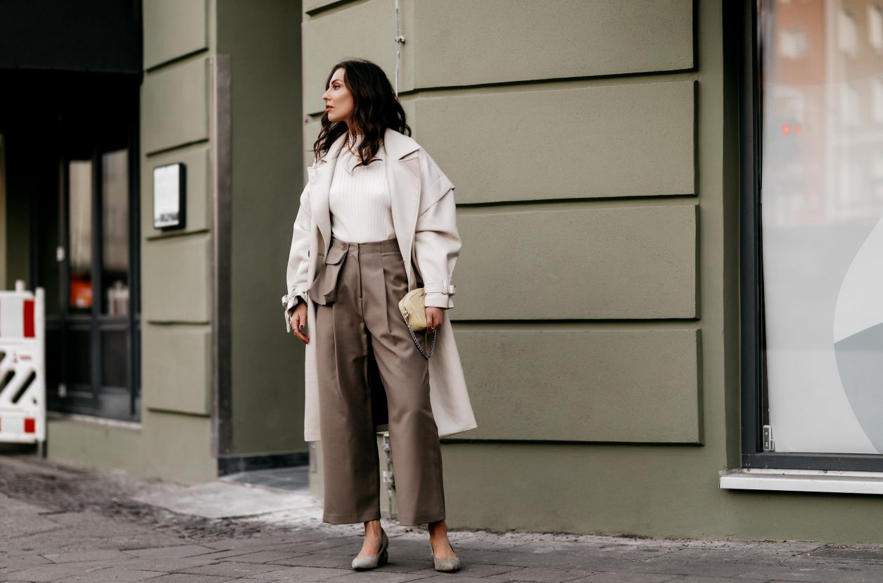 Spring Streetstyle outfit by Berlin fashion blogger Masha Sedgwick | Minimalistic, effortless cool, casual chic, wearing off white lack leather Apparis trench coat, off white Iris & Ink knit shirt, brown wide Frankie Shop pants with front pocket, lemon yellow WEAT crossbody mini bag, golden rings and necklaces, khaki green Charles & Keith pumps, hair style: black waves, photographer Jeremy Moeller 