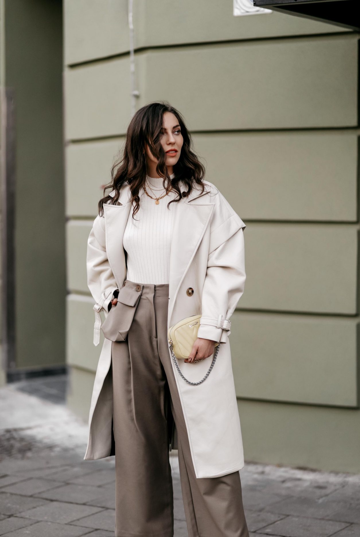 Spring Streetstyle outfit by Berlin fashion blogger Masha Sedgwick | Minimalistic, effortless cool, casual chic, wearing off white lack leather Apparis trench coat, off white Iris & Ink knit shirt, brown wide Frankie Shop pants with front pocket, lemon yellow WEAT crossbody mini bag, golden rings and necklaces, khaki green Charles & Keith pumps, hair style: black waves, photographer Jeremy Moeller 