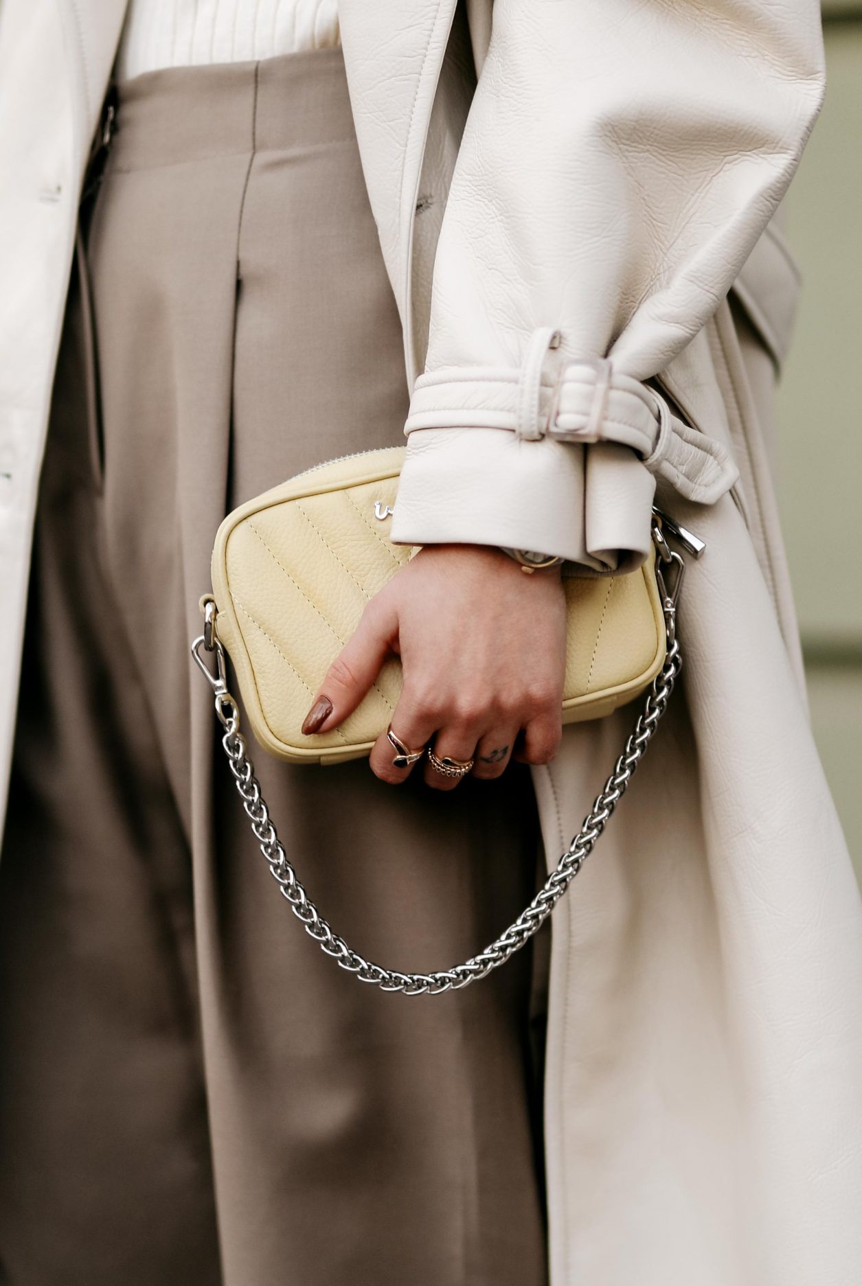 Spring Streetstyle outfit by Berlin fashion blogger Masha Sedgwick | Minimalistic, effortless cool, casual chic, wearing off white lack leather Apparis trench coat, off white Iris & Ink knit shirt, brown wide Frankie Shop pants with front pocket, lemon yellow WEAT crossbody mini bag, golden rings and necklaces, khaki green Charles & Keith pumps, hair style: black waves, photographer Jeremy Moeller 