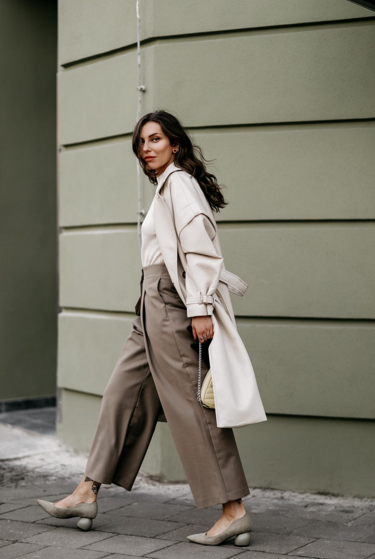 Spring Streetstyle outfit by Berlin fashion blogger Masha Sedgwick | Minimalistic, effortless cool, casual chic, wearing off white lack leather Apparis trench coat, off white Iris & Ink knit shirt, brown wide Frankie Shop pants with front pocket, lemon yellow WEAT crossbody mini bag, golden rings and necklaces, khaki green Charles & Keith pumps, hair style: black waves, photographer Jeremy Moeller 